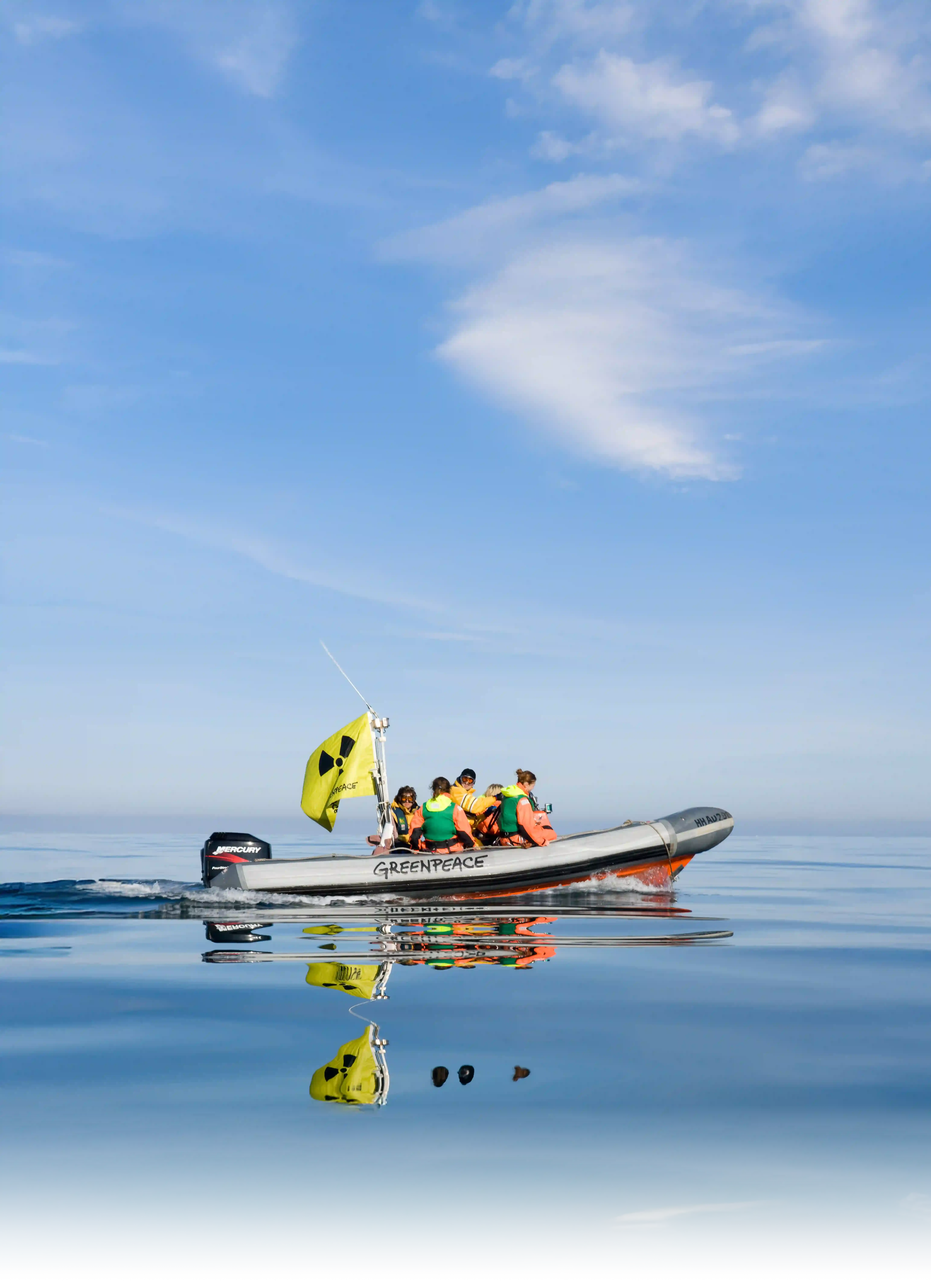 Large boat with yellow flag and Greenpeace logo on peaceful water under a cloudy sky